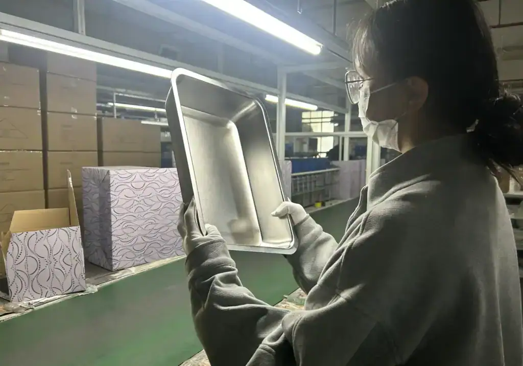 Operaio che ispeziona un vassoio in acciaio inossidabile in un ambiente industriale.