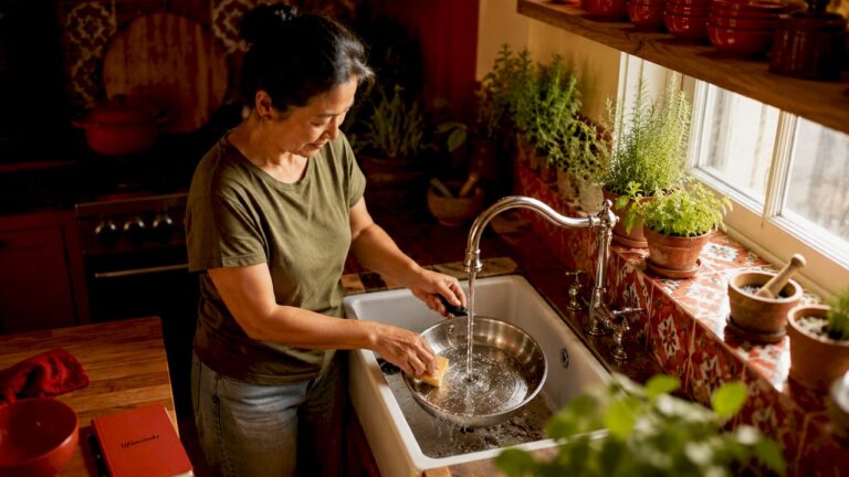 Woman cleaning stainless steel cookware in kitchen sink.
