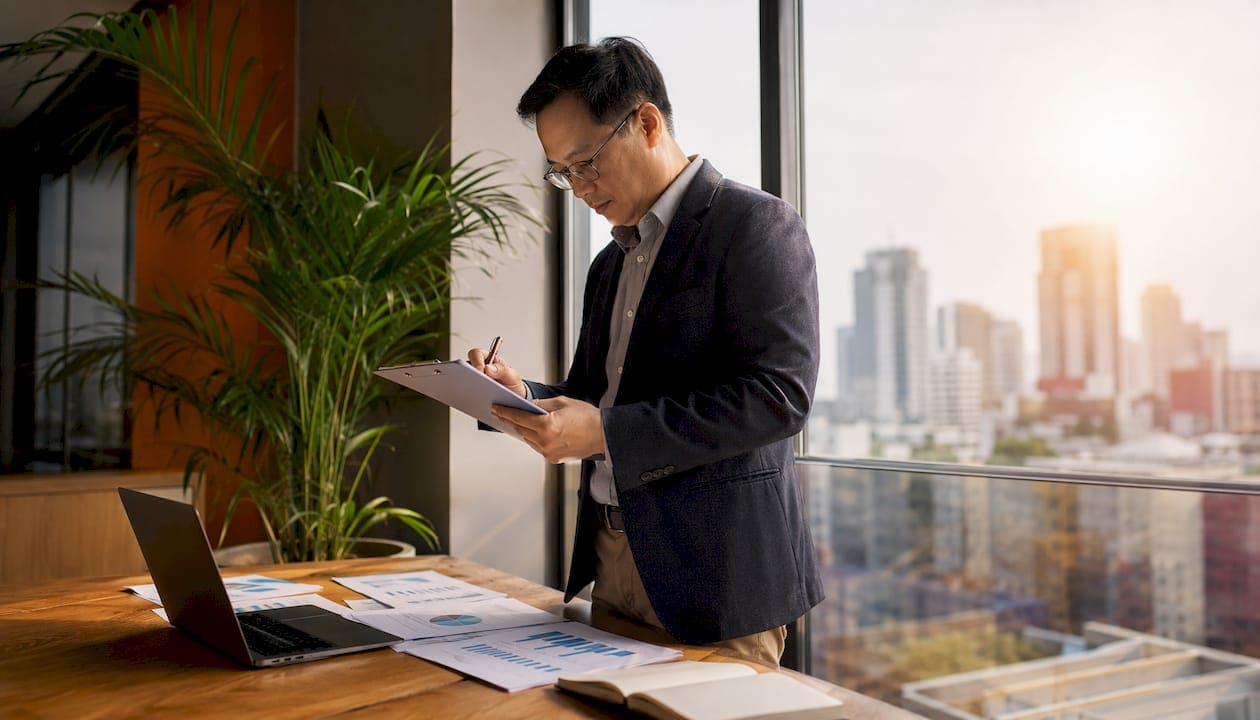 Businessman analyzing documents at desk with city view in background.