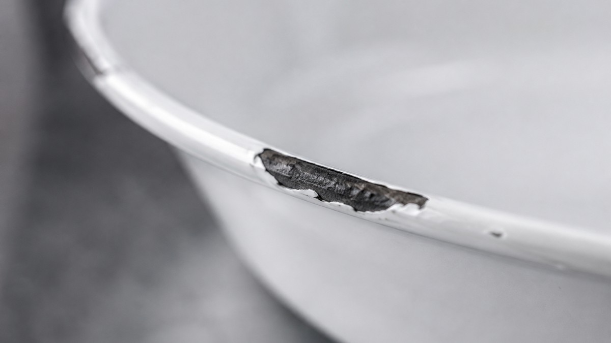Close-up of a chipped enamel rim exposing the bare cast iron underneath, the point where an enameled pot stops being non-reactive.