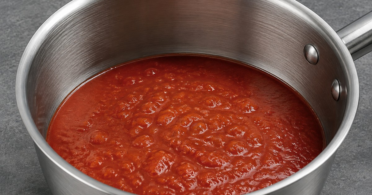 Tomato sauce simmering in a brushed stainless steel saucepan, the standard non-reactive cooking surface.